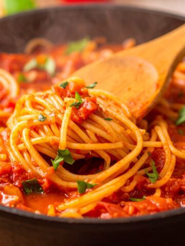 Slow-cooked crockpot spaghetti sauce in a ceramic pot with herbs and tomatoes.